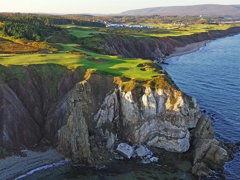 Aerial view of Cabot Cliffs Hole 16 — dramatic coastal cliffs with a lush green fairway overlooking the Atlantic Ocean